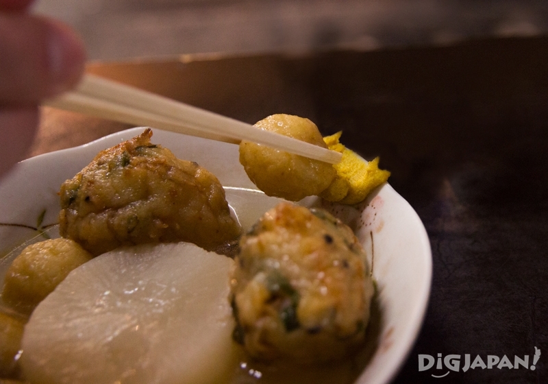 用筷子夾起關東煮，輕沾黃芥末